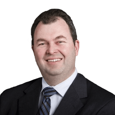 A man with short, dark hair in a black suit jacket and tie smiles at the camera.