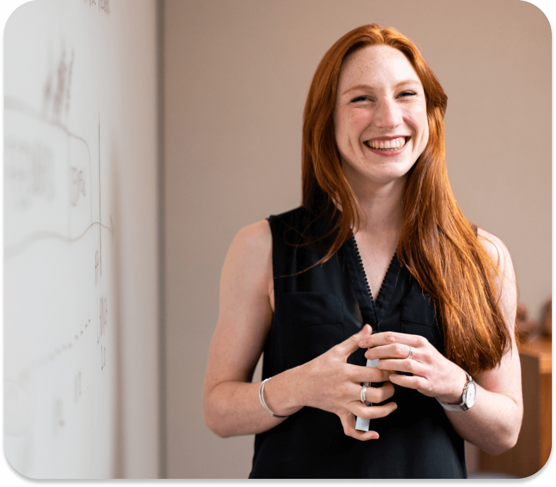 A confident woman stands in front of a white board.