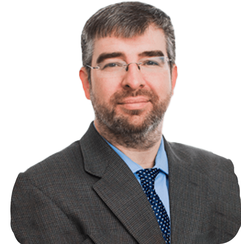 A man in a light grey suit jacket, blue shirt, and blue tie with white polka dots smiles at the camera.
