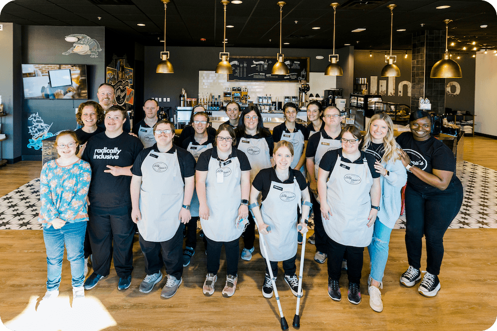 A group of Bitty a d Beau's employees posing in front of a cafe and smile at the camera.