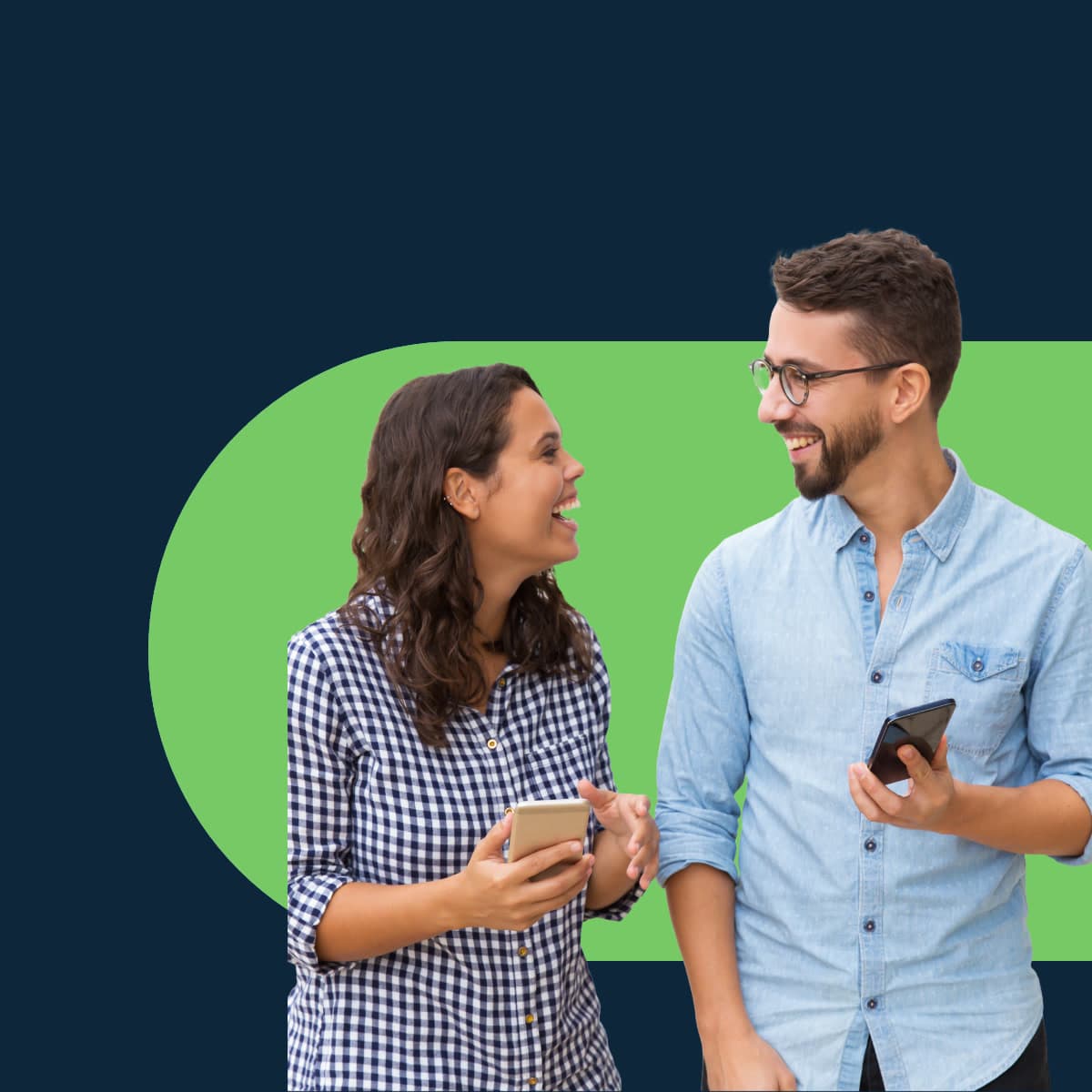A woman in a plaid shirt with long hair holds her phone and converses with a taller man with a beard and glasses wearing a plain blue button down shirt.
